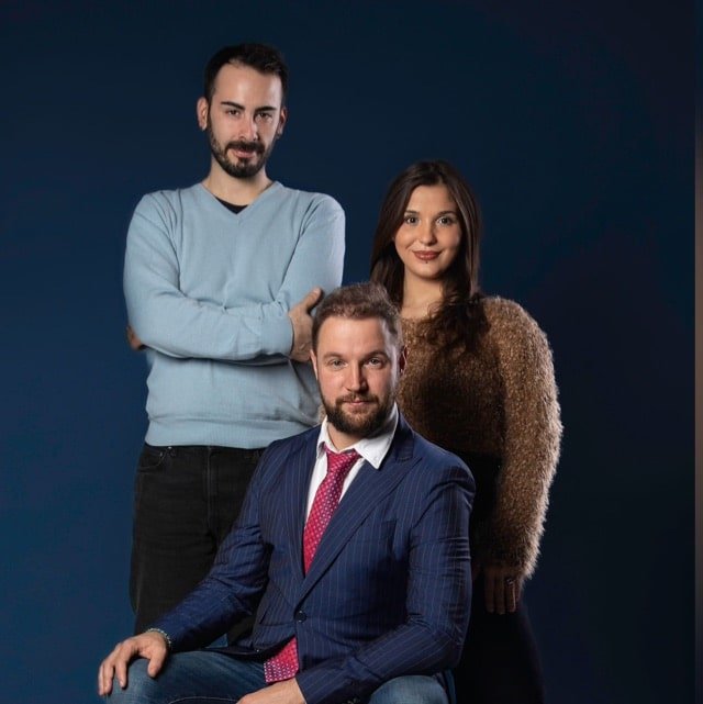 Drei Personen posieren für ein Foto vor einem blauen Hintergrund.