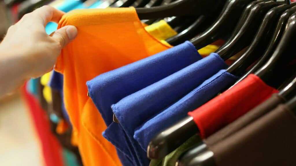 A person selecting a vibrant t-shirt from a shelf during a cruise to a resort.