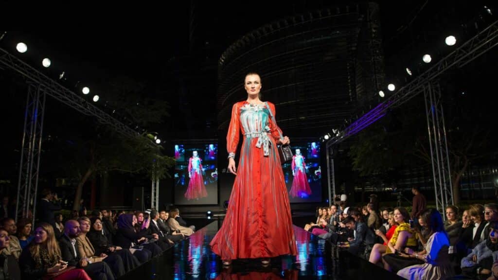 A woman in a red dress struts down the catwalk at night during a cruise collection at a resort.