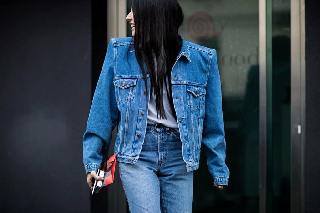 A woman in jeans and denim jacket walking down the street.
