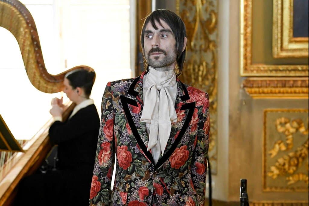 Un homme vêtu d'un costume à fleurs à côté d'une harpe, incarnant un symbole emblématique de la marque et un potentiel de contenu digne d'intérêt.