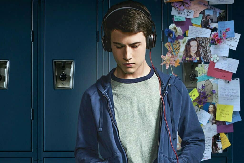 A young man with headphones is standing in front of the lockers, sporting a normcore style.