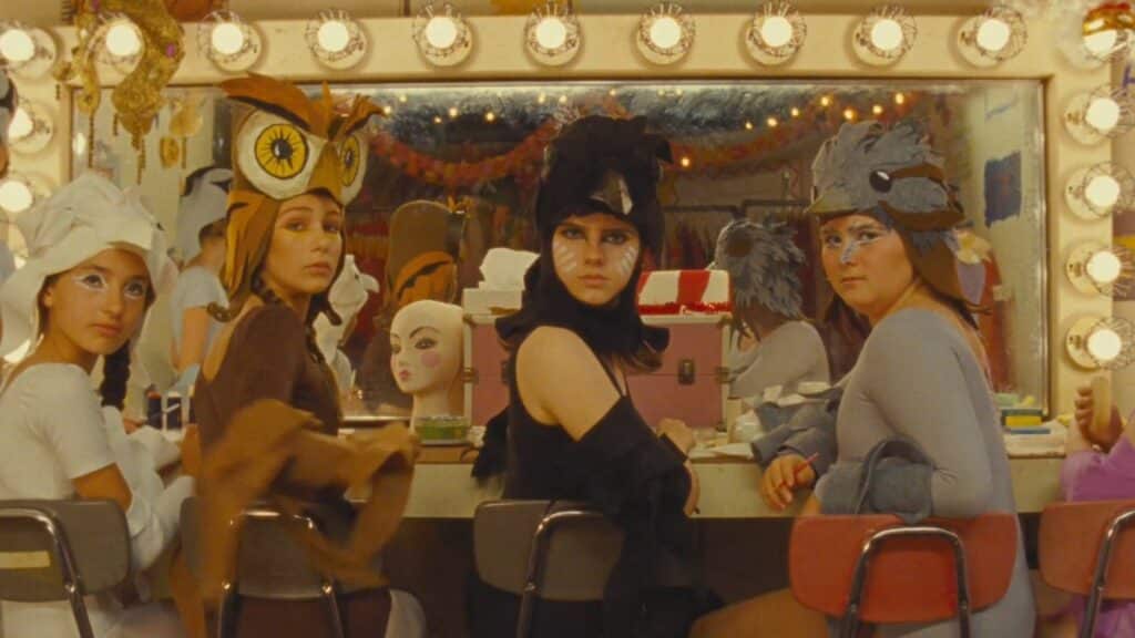 A group of women sit at a table, dressed as Gucci, in front of a mirror.