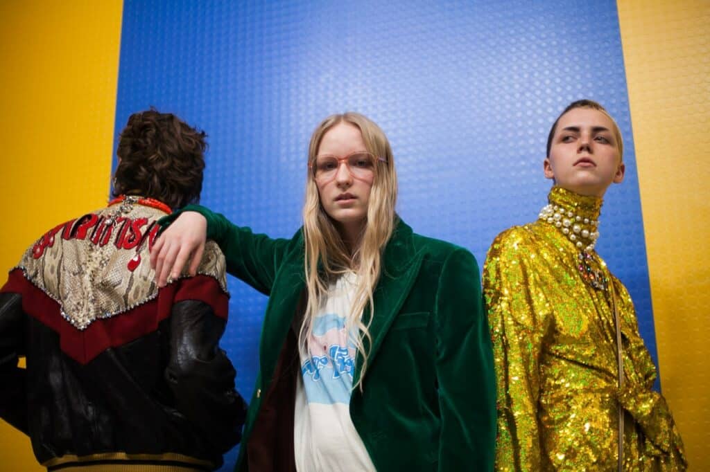 A group of people standing in front of a yellow wall in Gucci clothing.