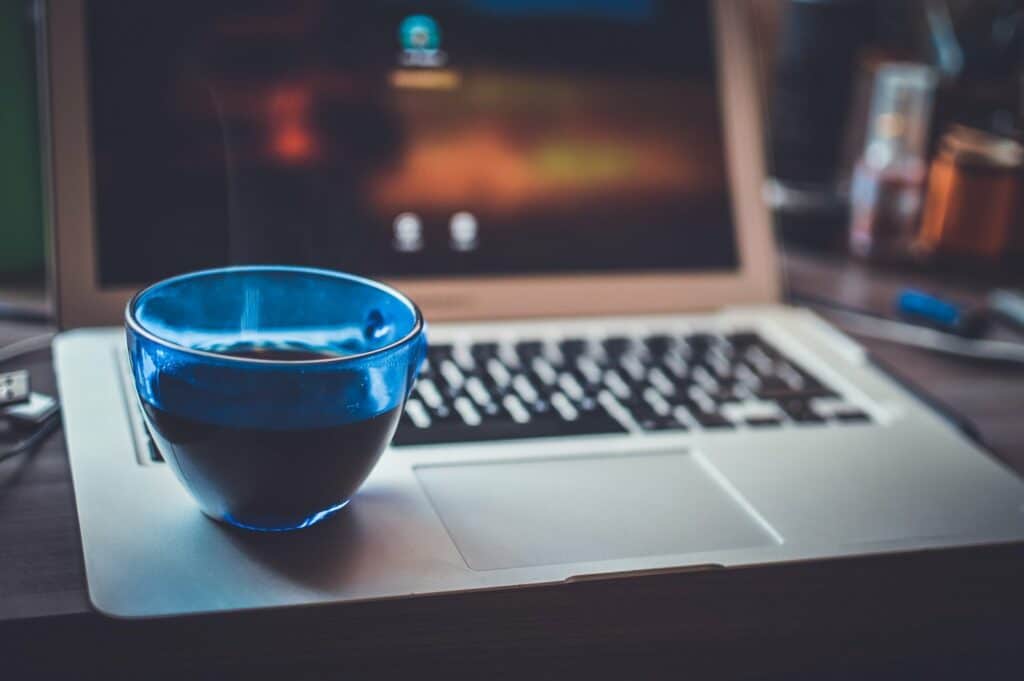 A laptop on a desk with a cup of coffee.