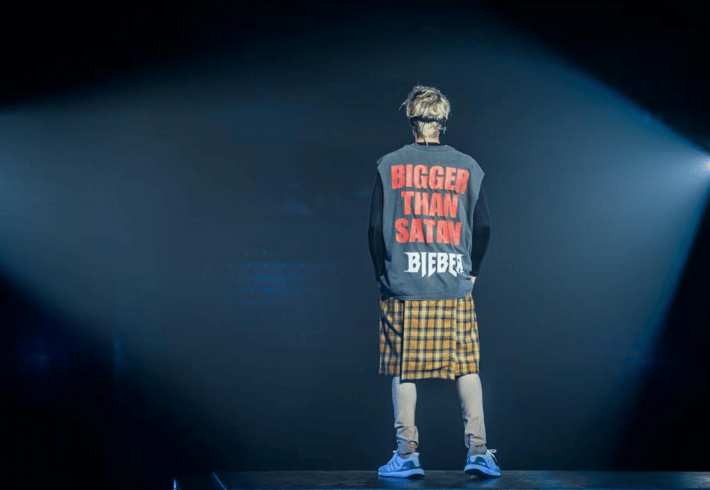 A man in a plaid shirt standing on a stage, showing how hip hop merged with metal as pop disrupted everything.