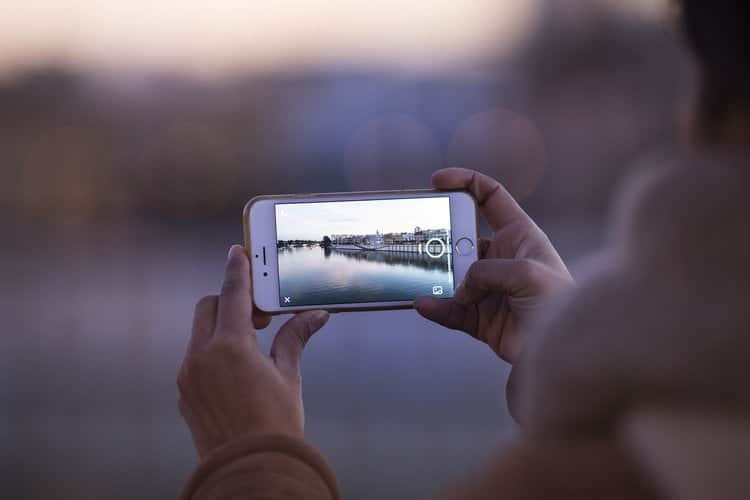 A woman is capturing a picturesque river on her smartphone.