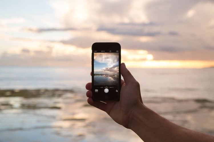 Une personne photographiant l'océan à l'aide d'un smartphone.