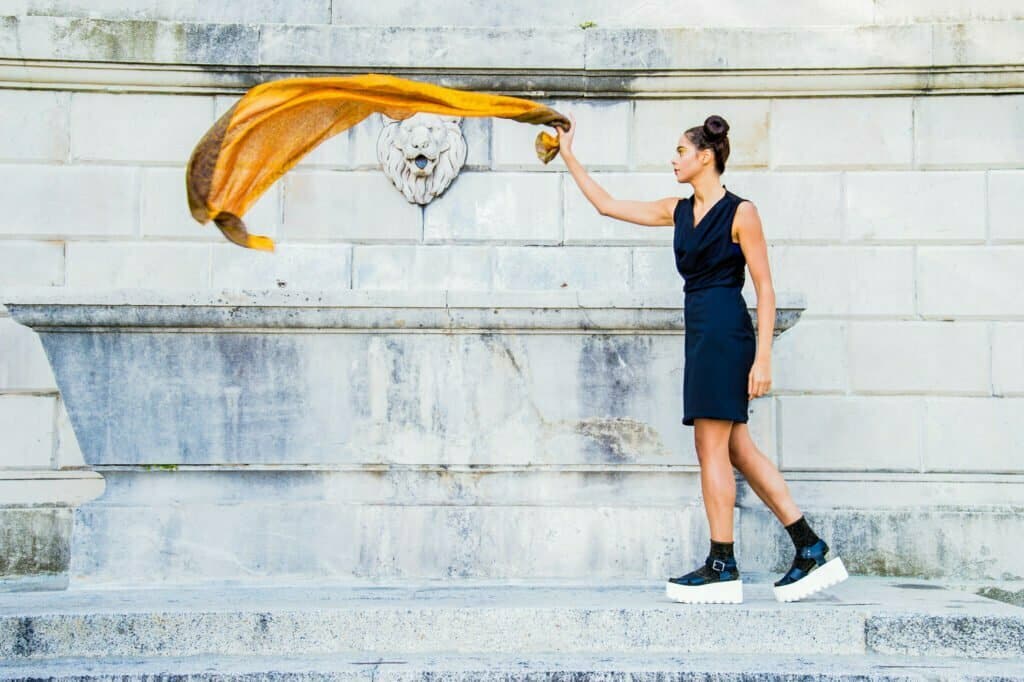 A woman holds her yellow scarf in front of a fountain at White Milano.