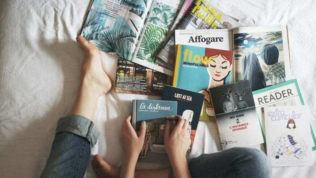 A person lying on a bed with magazines while preparing a press kit.