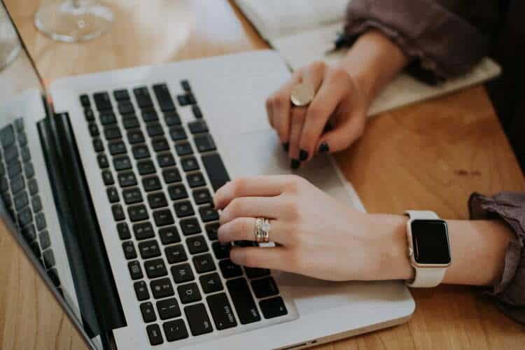 A woman writes on a laptop and wears an Apple Watch.