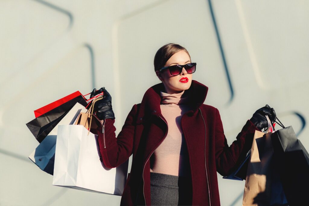 Una donna che mostra le borse della spesa davanti a un edificio, sottolineando la fusione del marchio di moda nell'era digitale.