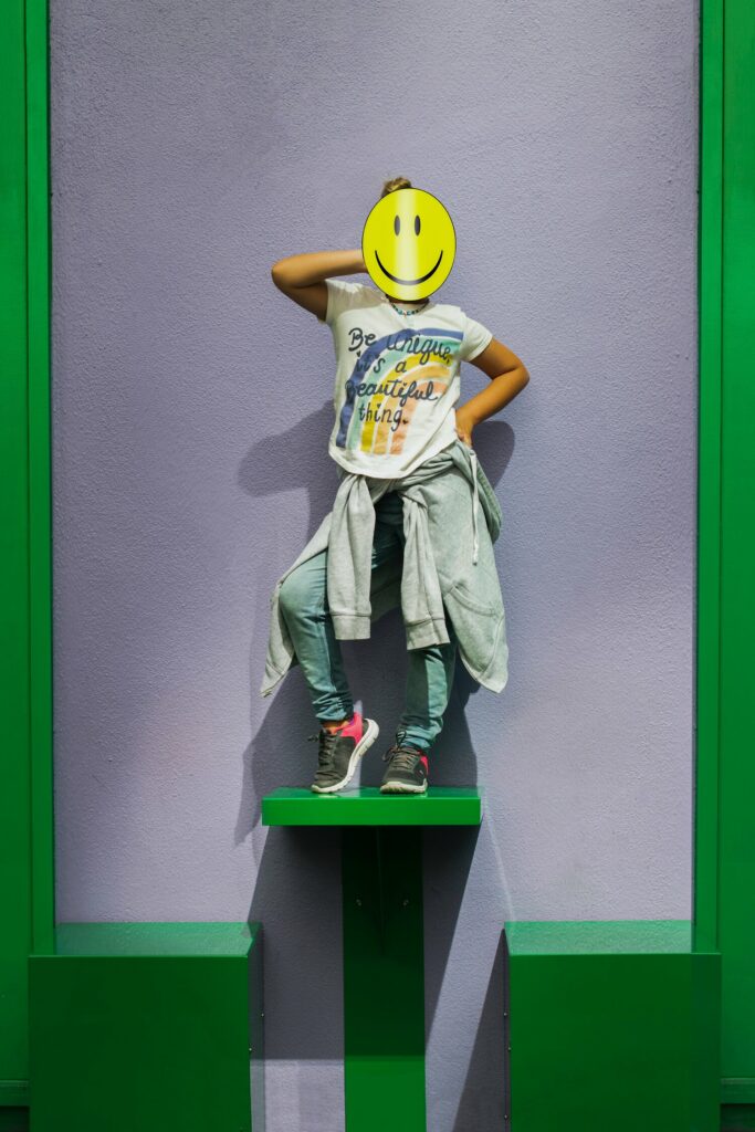 スマイルフェイスの少女が緑の壁の前に立ち、デジタル時代のファッション・ブランドを表現している。