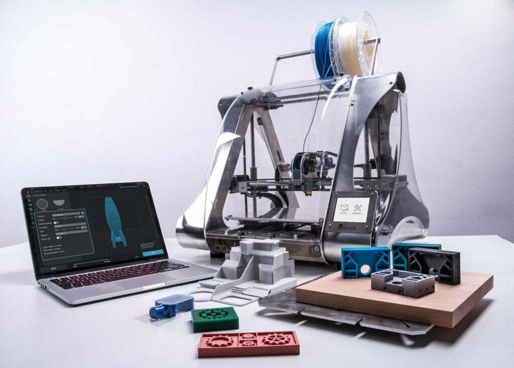 A 3D printer sits on a table next to a laptop, providing the essential steps to becoming a successful fashion designer.