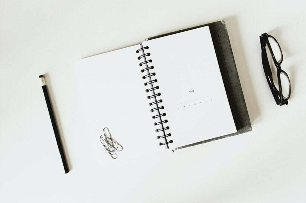 Un cuaderno y un bolígrafo sobre una superficie blanca, utilizados para la caza de la moda.