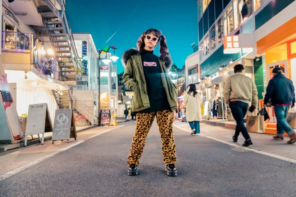 A woman in trousers with a leopard print hunts fashionably in a street at night.