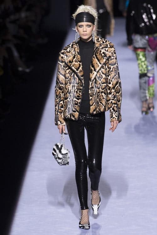 A woman struts down the AW 2018 catwalk in a leopard print jacket, embracing the 80s party atmosphere.