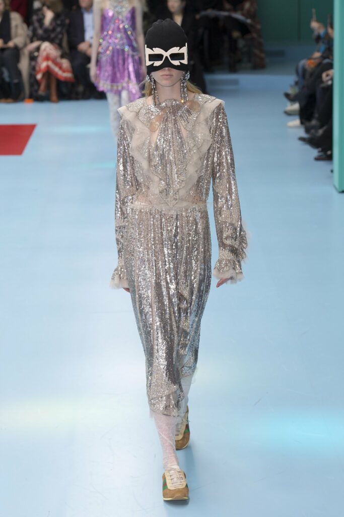 Una mujer con un vestido de lentejuelas desfila por la pasarela AW 2018, encarnando una estética de fiesta de los 80.