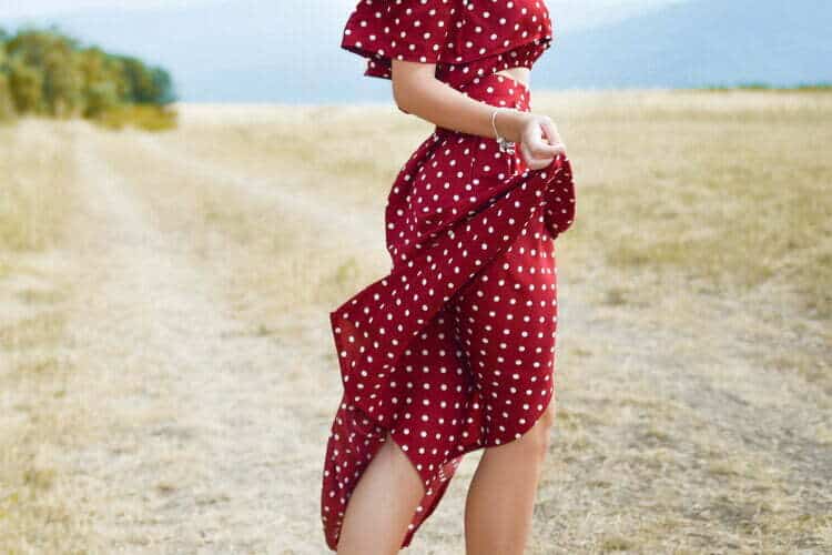Eine Frau in einem modischen Kleid steht auf einem Feldweg.