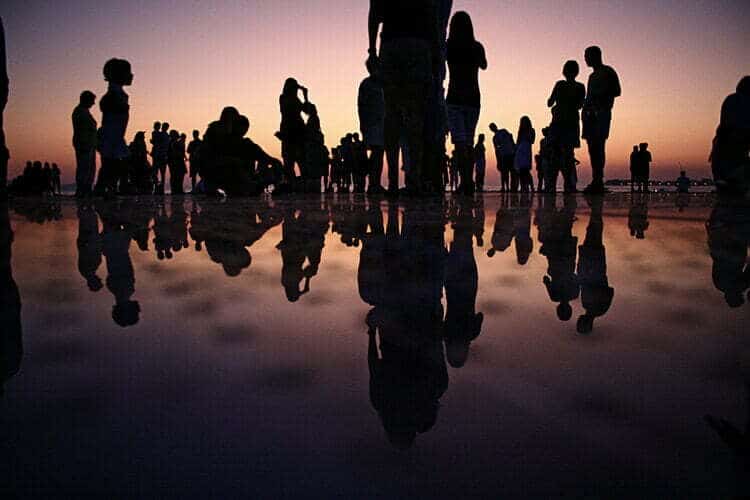 Un moodboard moda con un gruppo di persone in piedi su una spiaggia al tramonto.