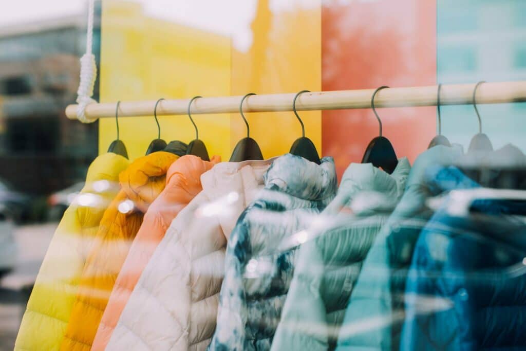 Coloridas chaquetas de nuevos diseñadores colgadas de un perchero frente a un escaparate.
