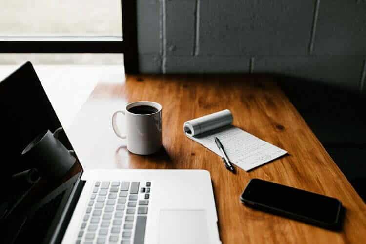 A laptop on a wooden desk with a cup of coffee in a fashionable setting.