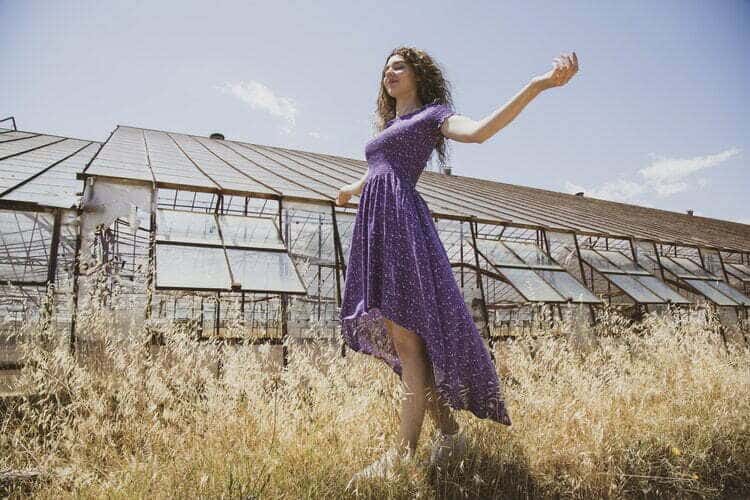 A woman in a purple dress in front of a greenhouse.