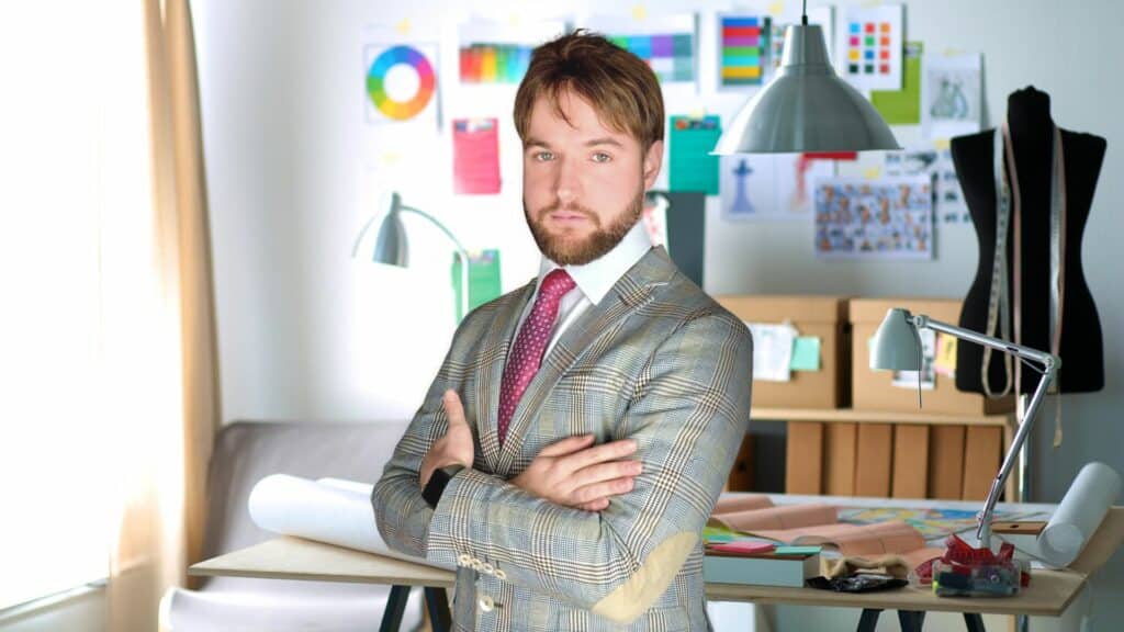 Un hombre con traje y corbata de pie en una oficina, que representa la oficina de estilo y la aspiración a convertirse en diseñador.