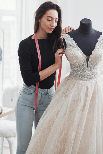 A woman is measuring a wedding dress on a mannequin in the style office.