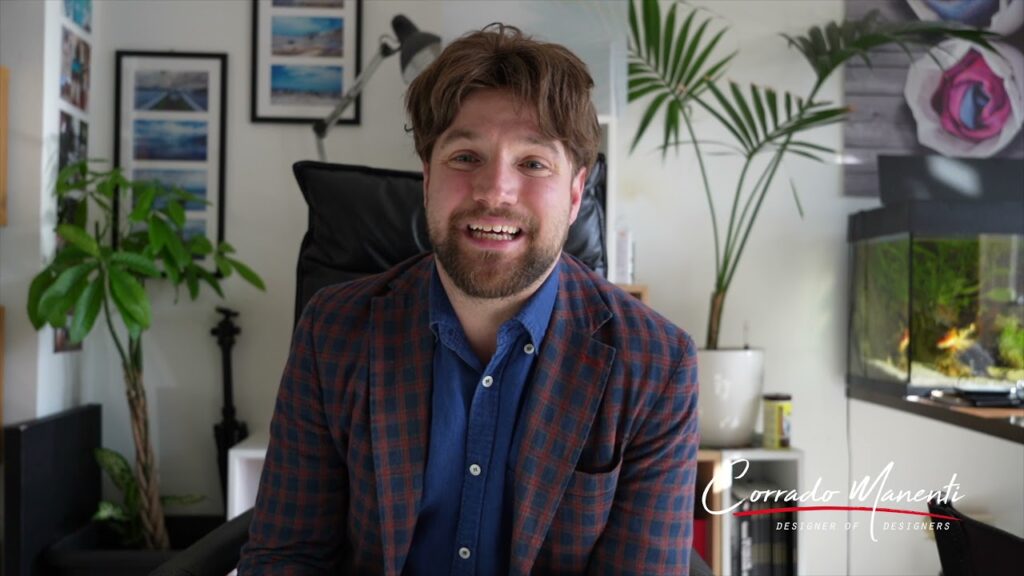 A man in a plaid shirt smiles in front of a plant.