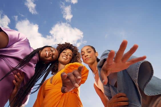 Eine Gruppe modischer Frauen posiert vor einem blauen Himmel, zeigt ikonische Modeartikel und fängt die Markttrends des Jahres 2023 ein.