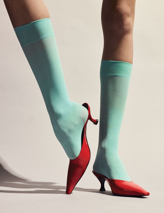 一位身着红色高跟鞋和绿松石套装的女士，紧跟 2023 年的时尚潮流。