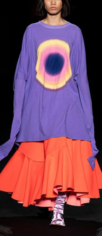 A woman in a purple shirt and orange skirt showing iconic fashion trends for the 2023 market.