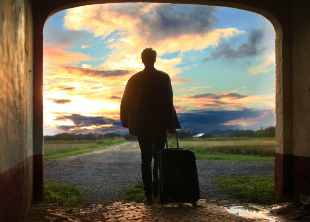 Un uomo con una valigia che attraversa un arco al tramonto, utilizzando una narrazione efficace nel settore della moda.