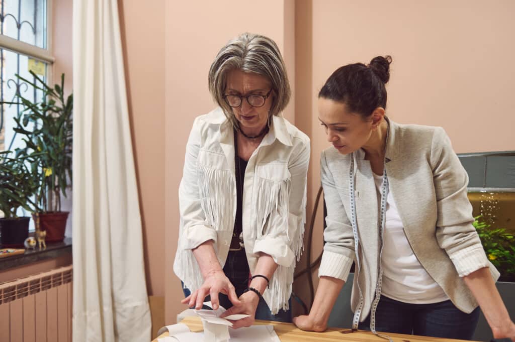 Deux femmes, dont une styliste de plus de 40 ans, examinent un document sur une table.