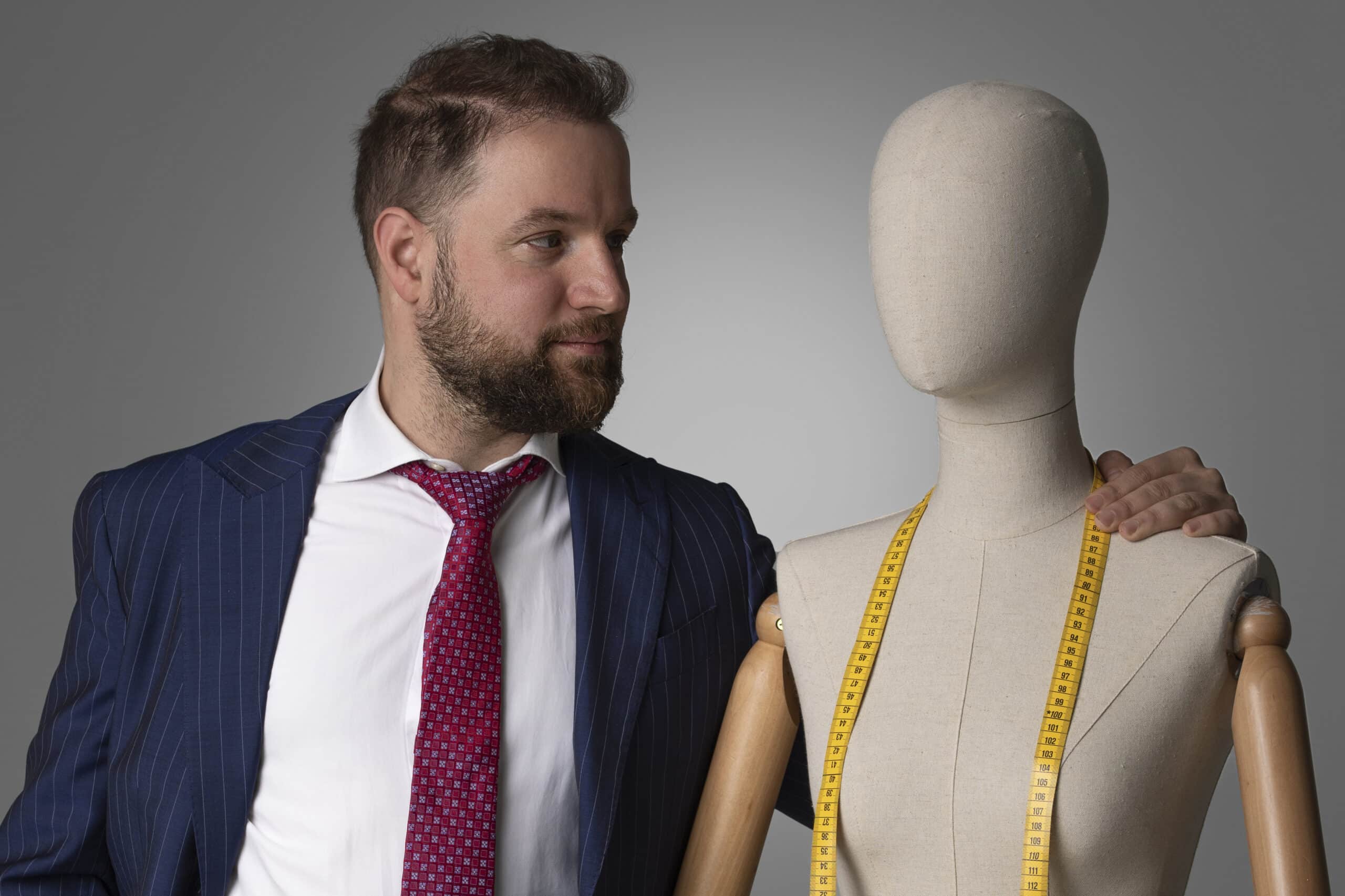 一名西装革履的男子站在一个人体模型旁，展示着他的时装品牌。