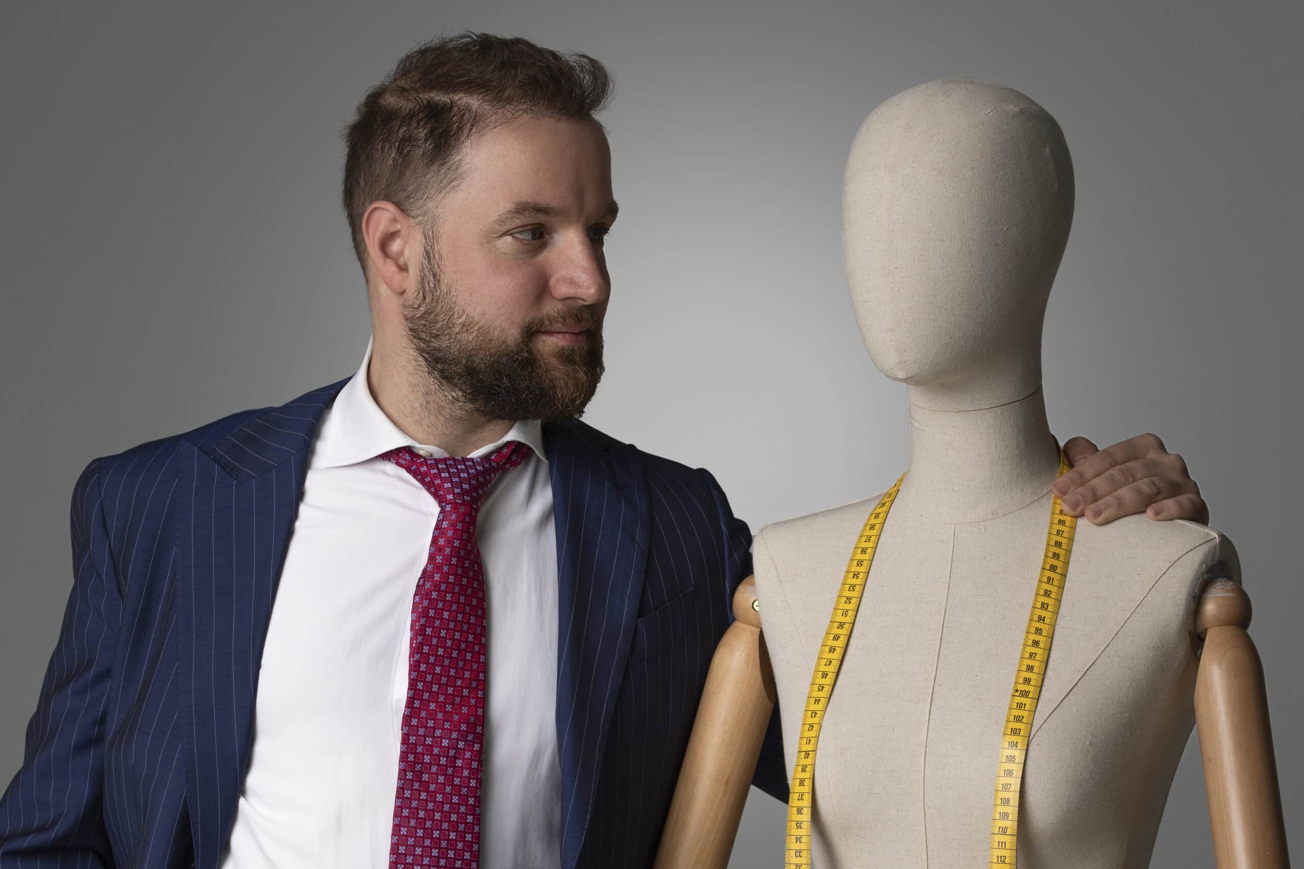 A man in a suit is standing next to a mannequin, displaying his fashion label.