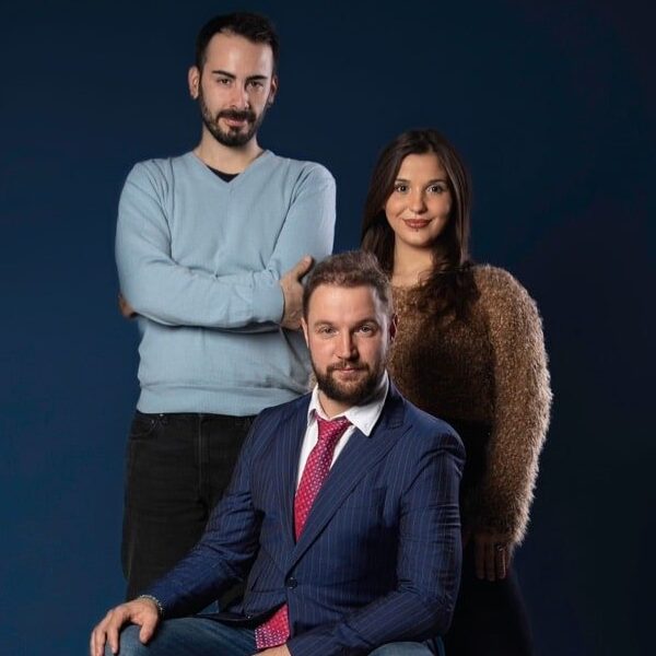 Tre persone in posa per una foto davanti a uno sfondo blu.