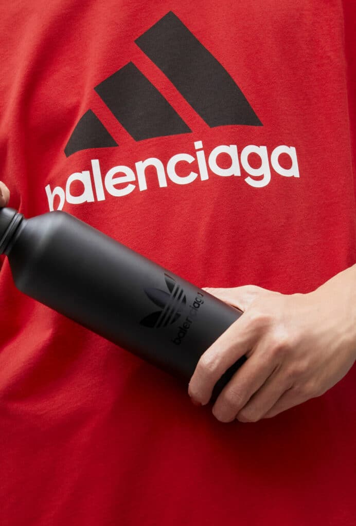 Une personne tenant une bouteille d'eau noire à la mode avec le mot Balenciaga, montrant la tendance de la mode de 2024.