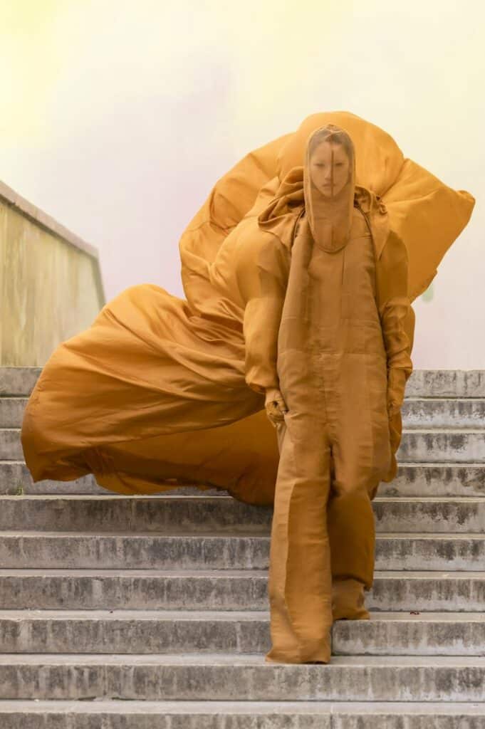 Un uomo con un cappotto giallo, che segue le ultime tendenze della moda del 2024, scende elegantemente le scale.