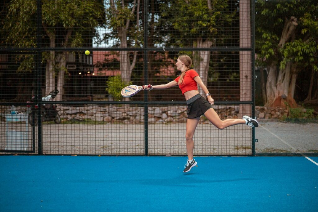 mujer con camiseta de tirantes roja y pantalones cortos negros sosteniendo raqueta de tenis