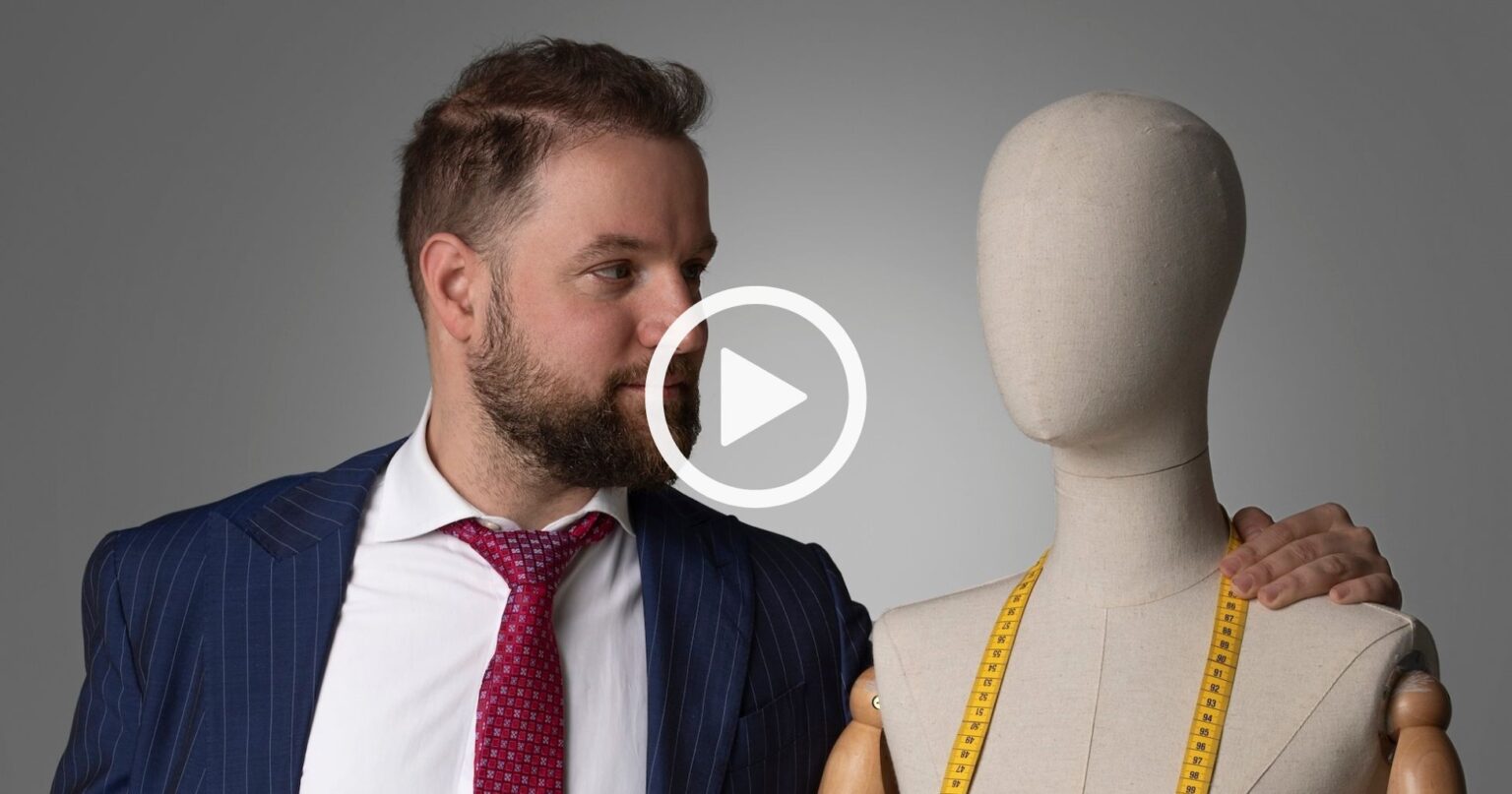 Un homme en costume-cravate rouge se tient à côté d'un mannequin, un mètre ruban drapé sur les épaules, incarnant l'essence du bureau de style, prêt à créer une marque de mode.
