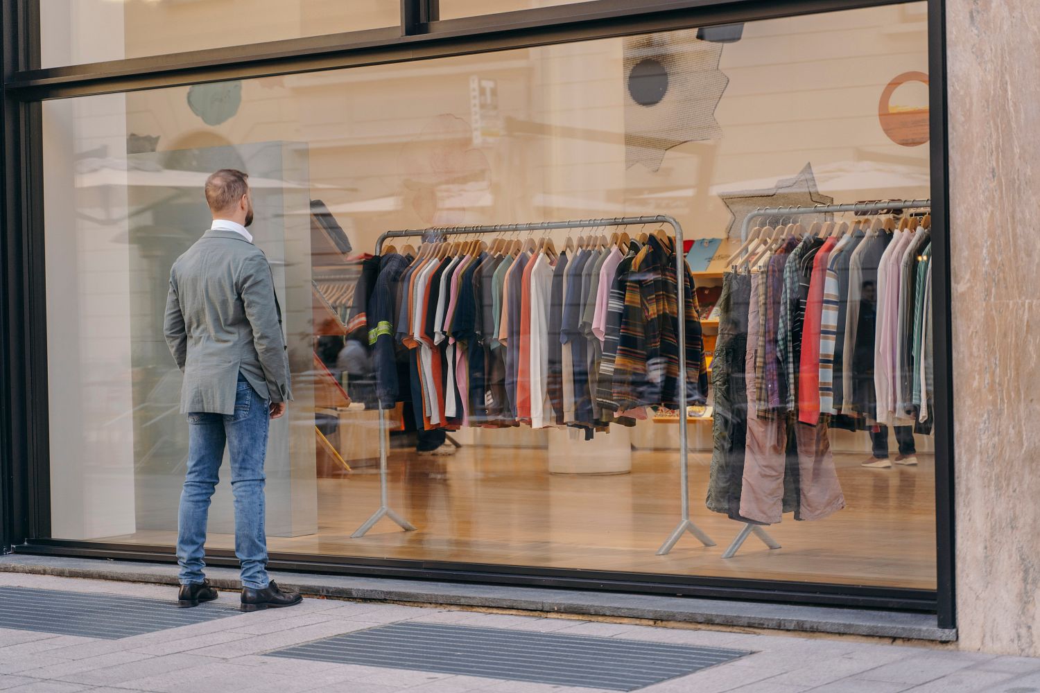 Personne regardant un étalage de vêtements à travers une grande vitrine, où diverses chemises sont présentées sur des étagères.