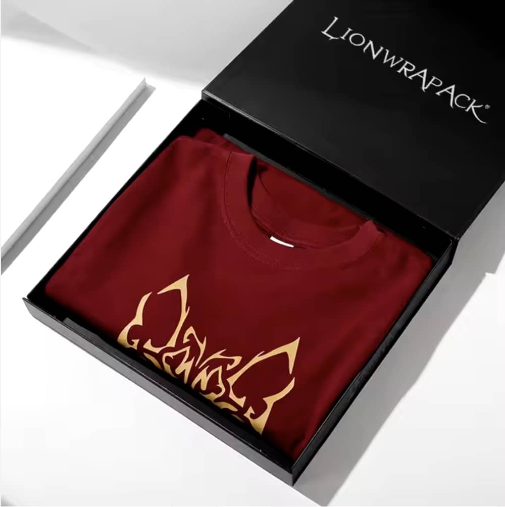 Un T-shirt rouge aux motifs dorés est soigneusement plié à l'intérieur d'une boîte noire portant le logo Lionwrapack.