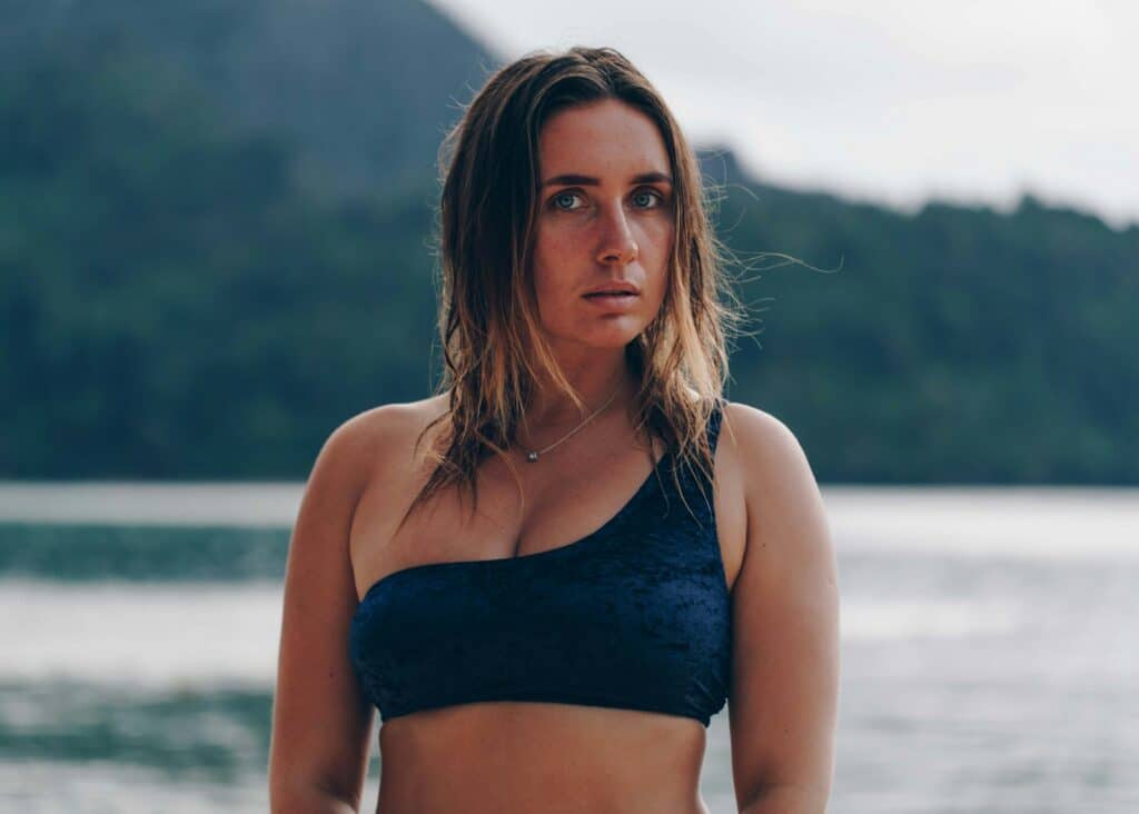 Photographie sélective d'une femme debout portant un soutien-gorge gris au bord de la mer pendant la journée.