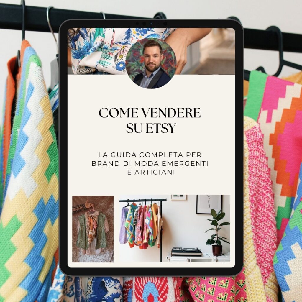 Un iPad che mostra una guida "come vendere su etsy" in italiano è tenuto di fronte a capi d'abbigliamento dai motivi colorati appesi a uno scaffale.