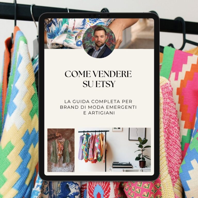 Un iPad che mostra una guida "come vendere su etsy" in italiano è tenuto di fronte a capi d'abbigliamento dai motivi colorati appesi a uno scaffale.