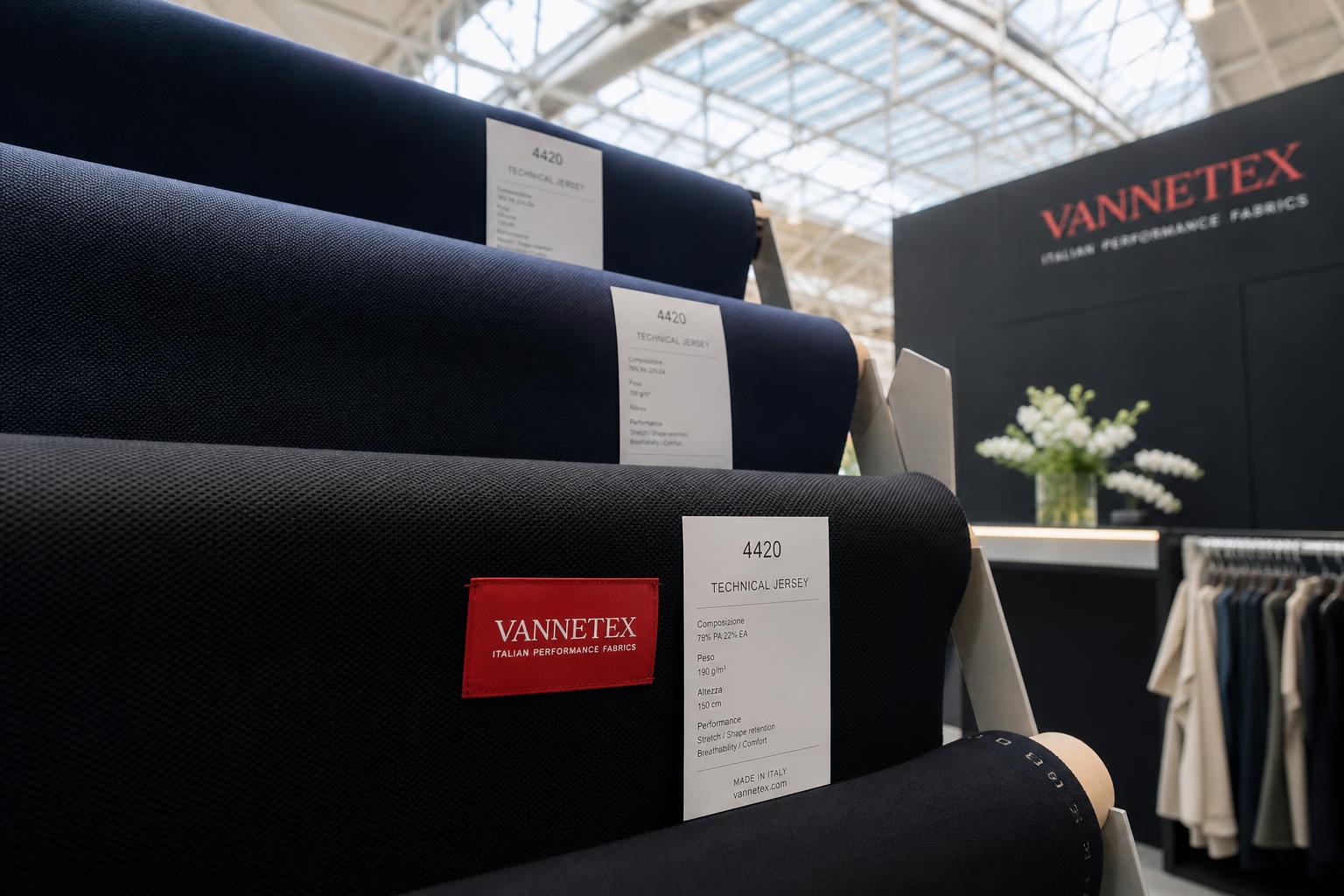 Wie man im Jahr 2026 eine Sportbekleidungsmarke gründet: HYROXs Lektion für aufstrebende Designer 1 Stand fornitore tessuti tecnici jersey navy e nero in una fiera tessile italiana, contesto Milano Unica activewear